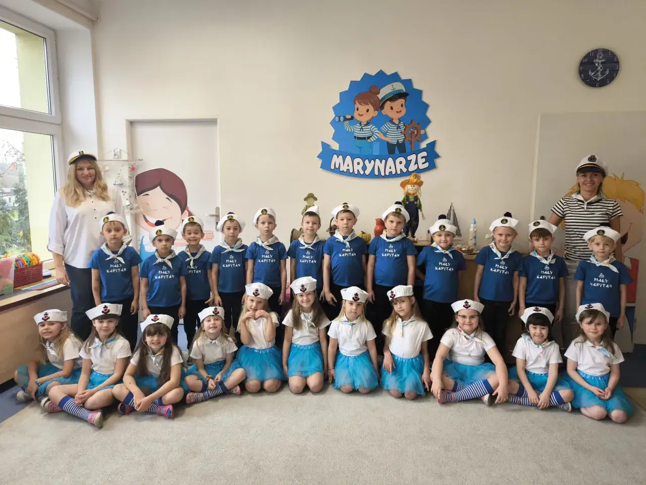 Dzieci w strojach marynarskich, gotowe do zabawy w marynarza. Na ścianie napis