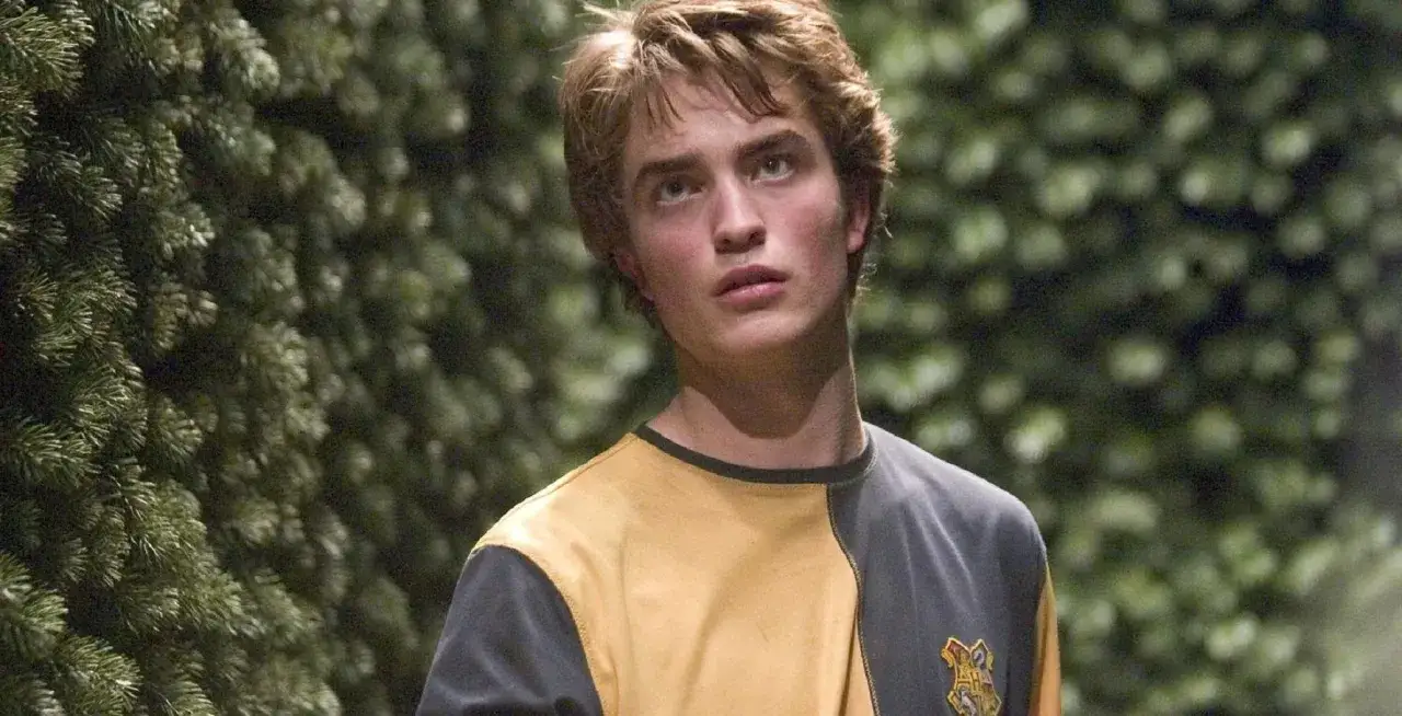 Cedrik Diggory, dumny reprezentant Hufflepuff, w swoim ż&oacute;łto-szarym swetrze, wygląda na zamyślonego wśr&oacute;d zieleni.