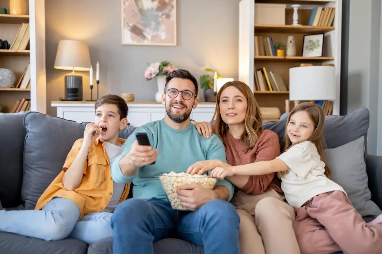 Rodzina ogląda wzruszające filmy familijne, zajadając popcorn. Ojciec trzyma pilota, a dzieci z zaciekawieniem patrzą na ekran.