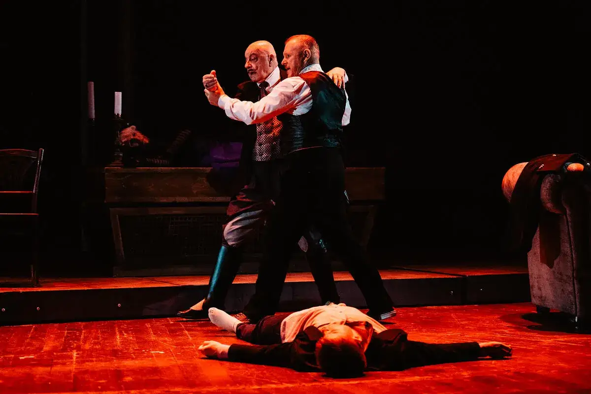 Dw&oacute;ch mężczyzn tańczy tango, podczas gdy trzeci leży na scenie. Dramatyczne tango streszczenie.