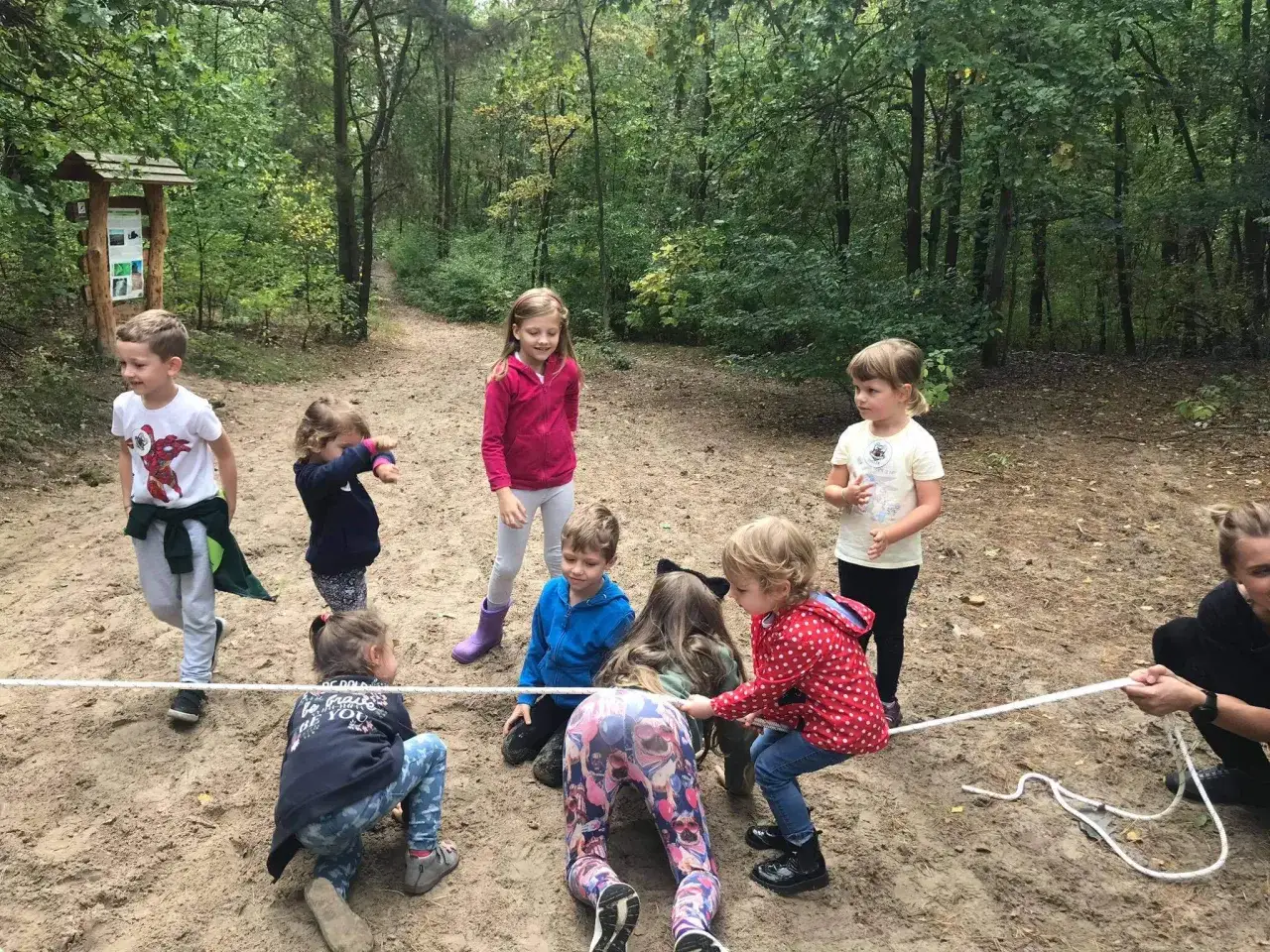 Dzieci biorą udział w zabawach integracyjnych na świeżym powietrzu, ciągnąc linę w lesie.