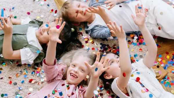 Radosne dzieci leżą na dywanie wśród kolorowych konfetti, ciesząc się wspólnymi zabawami integracyjnymi.