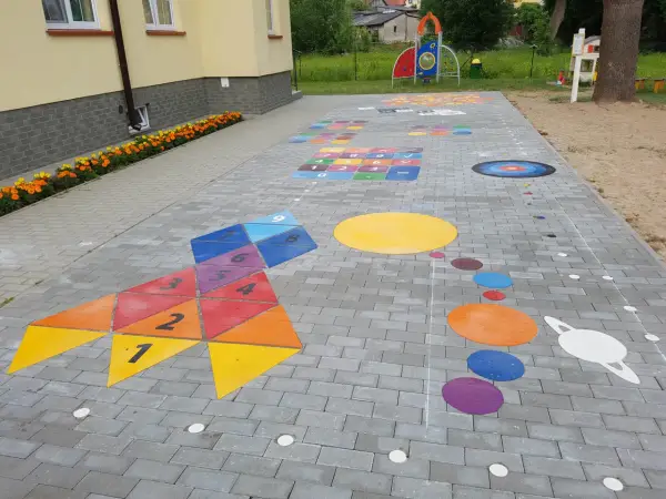 Kolorowe gry plenerowe na placu zabaw: rakieta z liczbami, układ planet i plansza do gry.