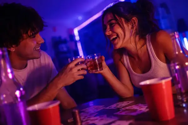 Para dwojga śmieje się, wznosząc toasty podczas gry w karty. Idealne gry alkoholowe dla 2 osób na wieczór.