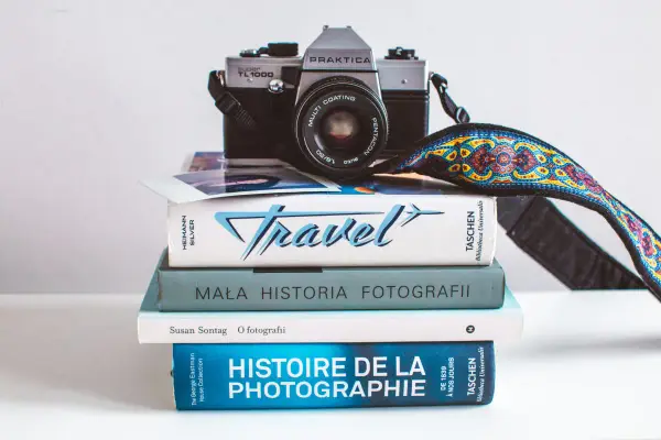 Stos książek o fotografii, w tym "Mała historia fotografii" i "Histoire de la photographie", z aparatem Praktica na górze.