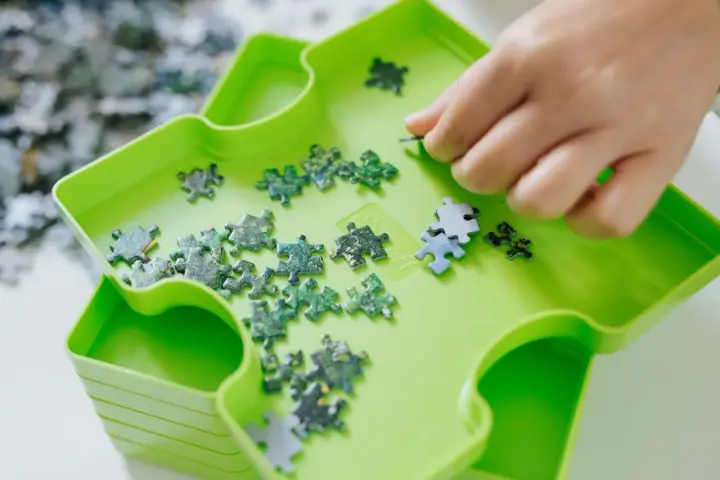 Dłoń układa zielone i niebieskie elementy układanki. To świetna zabawa, by układać puzzle po angielsku.