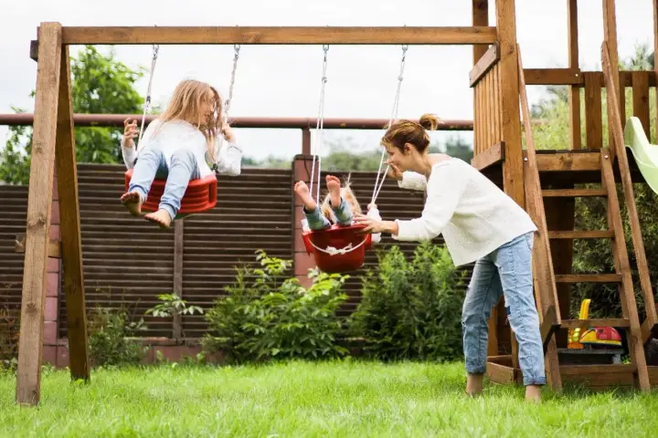 Mama pcha dzieci na huśtawkach, radosne zabawy dla dzieci na dworze.